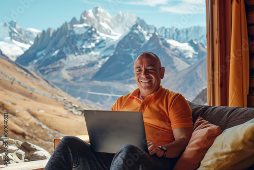 Man working remotely from a wooden cabin, with a laptop. Beauty mountains through a large window. Productivity with the tranquility of nature.