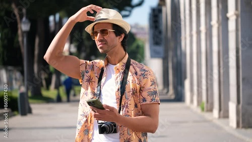 Indian tourist man is lost, looking at a map in his smartphone to find the way in the city of Madrid, Spain. He is wearing a straw hat and sunglasses