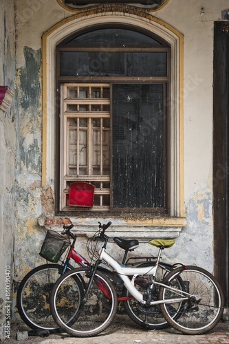 Old rusty bicycles parked in front of window of abandoned house.