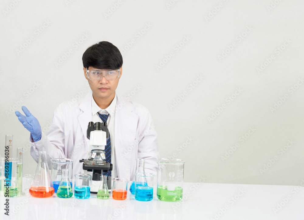 Portrait asian man student scientist Wearing a doctor gown in the lab looking hand at chemist. caused by mixing reagents in scientific research laboratories with test tubes and microscope on the table Portrait asian man student scientist Wearing a doctor gown in the lab looking hand at chemist. caused by mixing reagents in scientific research laboratories with test tubes and microscope on the table