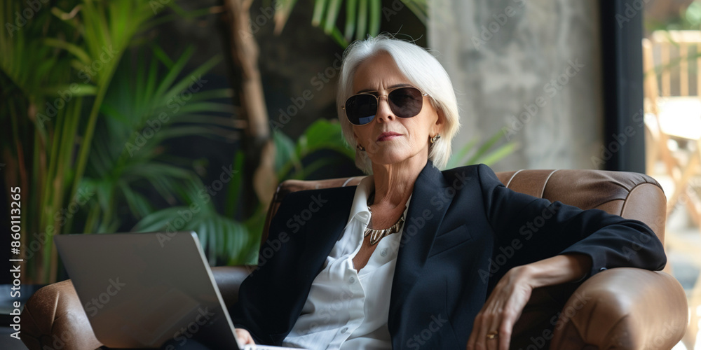Freelance online remote work freedom concept. Senior businesswoman in suit working on computer while travelling. Businesslike woman using laptop on tropical luxury hotel resort. Freelance online remote work freedom concept. Senior businesswoman in suit working on computer while travelling. Businesslike woman using laptop on tropical luxury hotel resort.