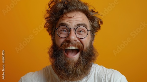 A cheerful bearded man wearing round glasses and a white shirt smiles widely against a bright orange background, exuding joy and positivity in the portrait.