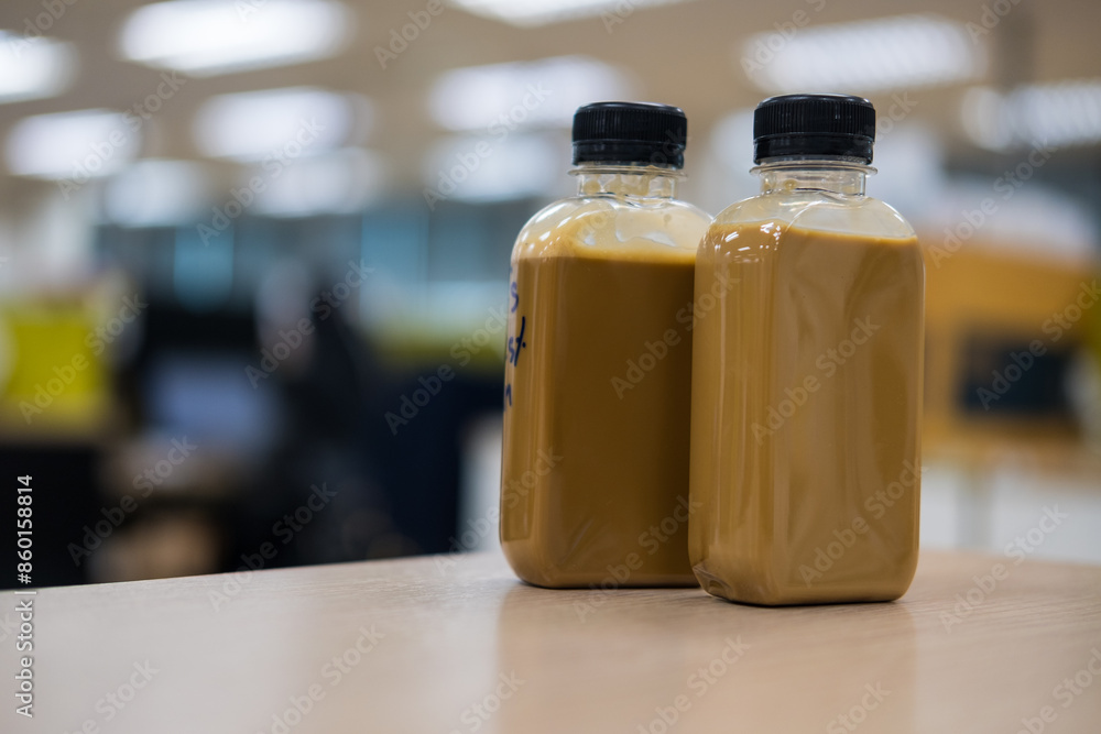 A plastic two bottles of iced coffee latte on wood table at office background. A plastic two bottles of iced coffee latte on wood table at office background.