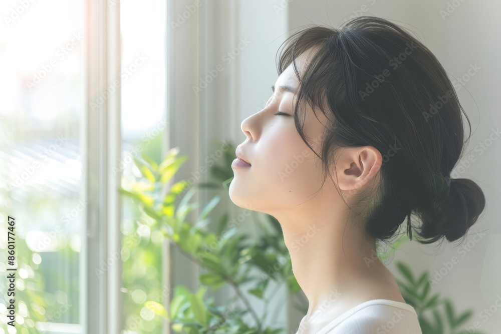 A young woman with dark hair stands by a window, eyes closed, taking a deep breath A young woman with dark hair stands by a window, eyes closed, taking a deep breath