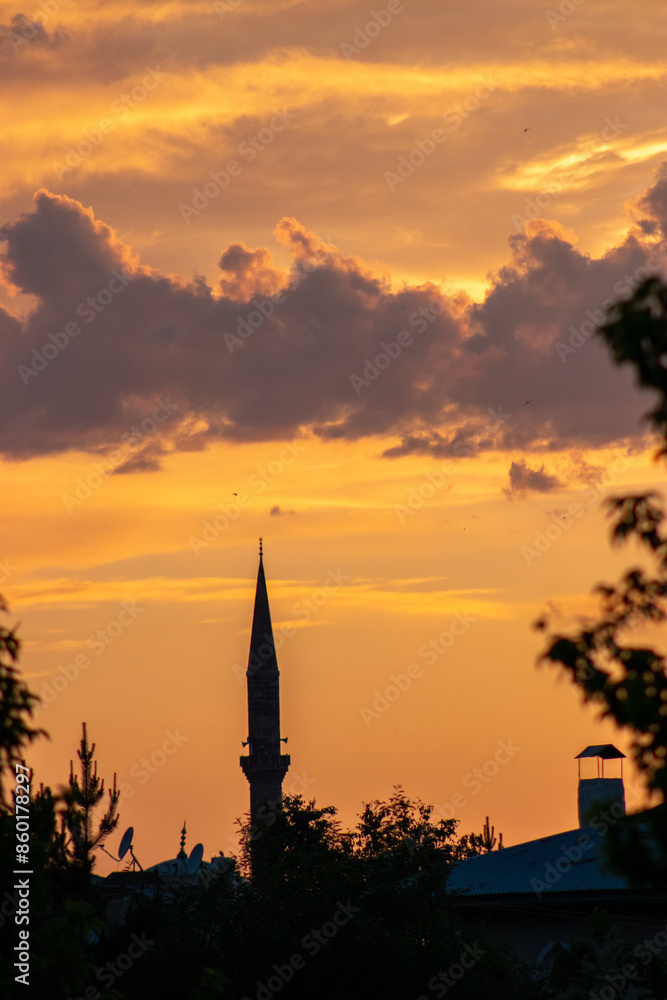 Fototapeta premium Silhouette of a mosque minaret against a vibrant sunset sky, symbolizing spirituality and tranquility.
