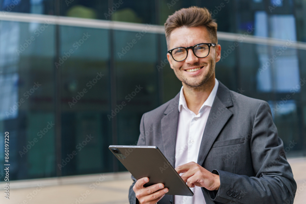 A smiling businessman in a suit uses a tablet, standing confidently in a modern urban environment. A smiling businessman in a suit uses a tablet, standing confidently in a modern urban environment.