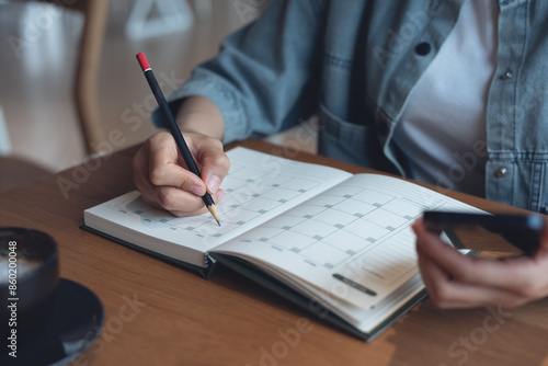 Event planner timetable agenda plan on year 2024 schedule event. Business woman checking planner on mobile phone, taking note on calendar desk on office table. Calendar event plan, work planning photo