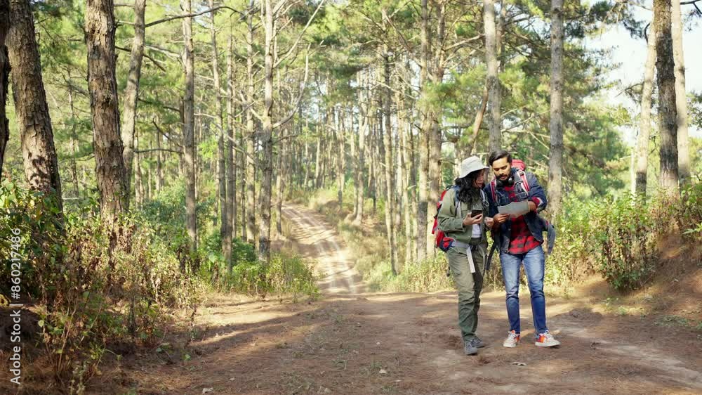 Asian couple backpacker enjoy active outdoor lifestyle hiking at forest together on summer holiday vacation. Man and woman using online map navigation on smartphone during walking mountain dirt road. Asian couple backpacker enjoy active outdoor lifestyle hiking at forest together on summer holiday vacation. Man and woman using online map navigation on smartphone during walking mountain dirt road.