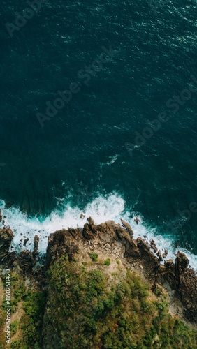 Aerial view of Mawun Beach, Lombok, highlighting waves crashing against rocky cliffs and lush greenery, showcasing the rugged natural beauty of this secluded tropical paradise. 