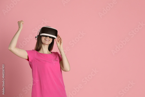 Smiling woman using virtual reality headset on pink background, space for text © New Africa