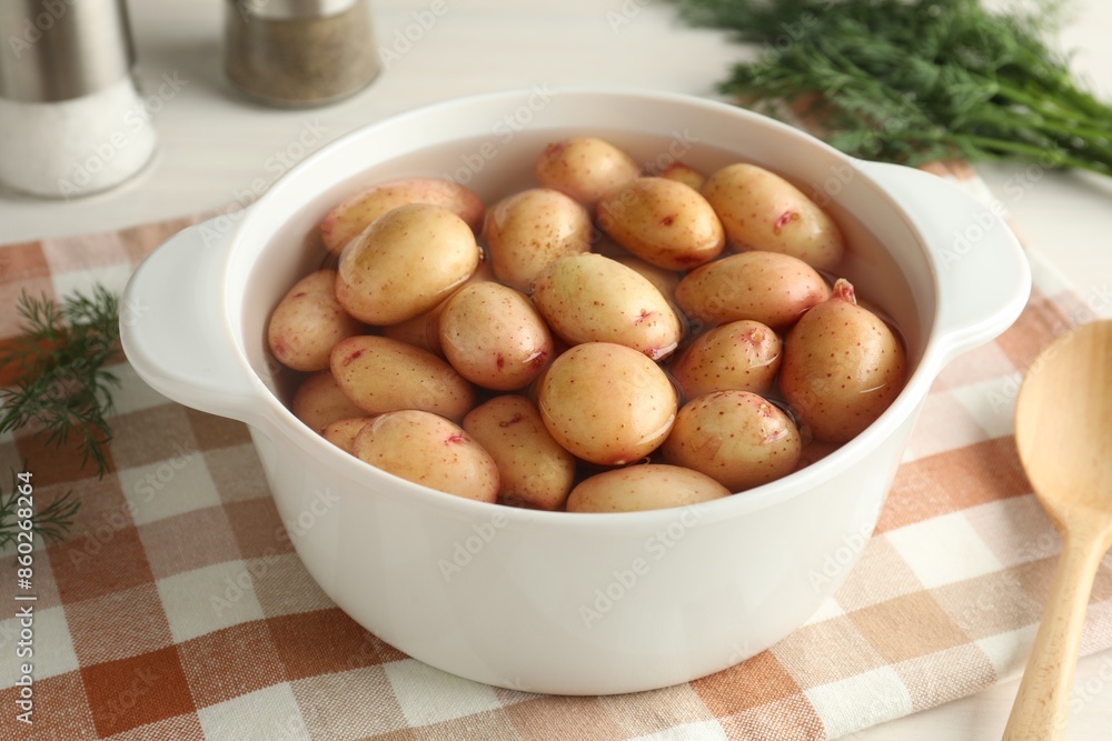 Raw potatoes in pot with water, dill and spoon on table Raw potatoes in pot with water, dill and spoon on table
