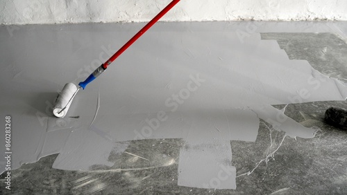 Varnishing of concrete floors. Apply primer to the surface using a roller brush. Close-up. Applying paint with a roller to a concrete floor. A man paints a concrete floor with a paint roller. © Ruslan