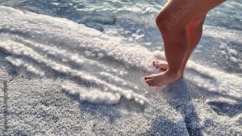 SLOW MOTION walk peaceful barefoot along serene sandy beach shoreline of Dead Sea in Jordan with calm waves and clear water. Providing sense of relaxation and serenity amidst tranquil seaside nature