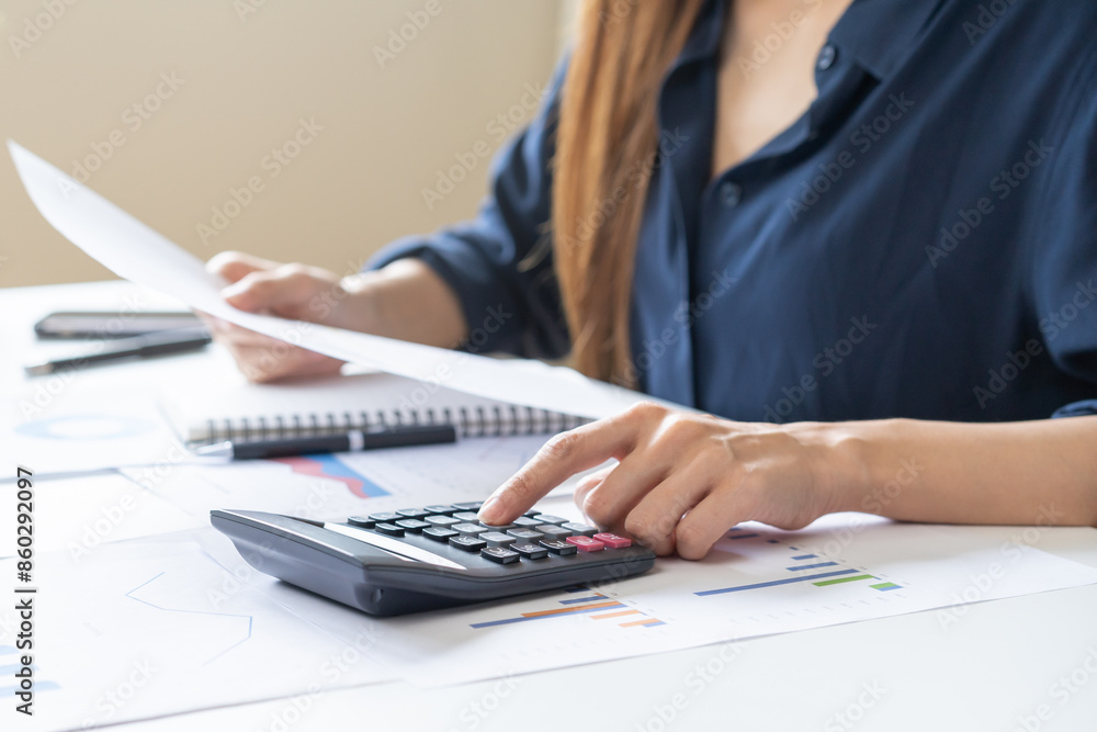 Account finance, asian young business woman hand use calculator for calculate budget, cost and income of company from charts, reports paperwork, plan spend money expenses, working on desk at home. Account finance, asian young business woman hand use calculator for calculate budget, cost and income of company from charts, reports paperwork, plan spend money expenses, working on desk at home.