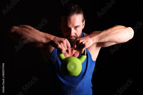 muskulöser Mann mit Kettlebell vor Gesicht vor schwarzem Hintergrund photo