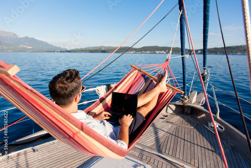 Working in traveling. Freelancer using laptop, Internet. Business man with computer in beach hammock. Sea summer vacation on yacht, workation lifestyle. Digital nomad workplace in nature outdoors