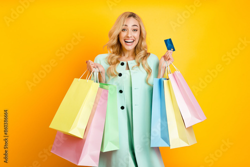 This image shows a woman holding multiple shopping bags and a credit card in front of a bright yellow background. She is smiling and appears happy with her purchases.