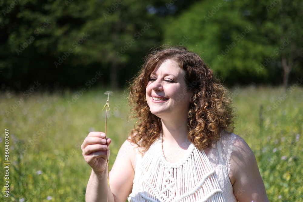 Frau im weissen Sommerkleid pustet eine Pusteblume weg, 1 Keim übrig
