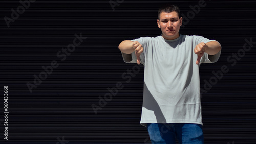 Young man making disapproval hand sign on black background, dislike, negative 