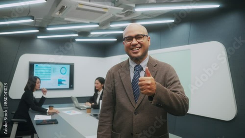 Wallpaper Mural Happy professional Asian businessman wearing a brown suit standing in front of blur colleagues meeting in the background. He thumbs up and smiling to camera. Entrepreneur leadership concept. Torontodigital.ca