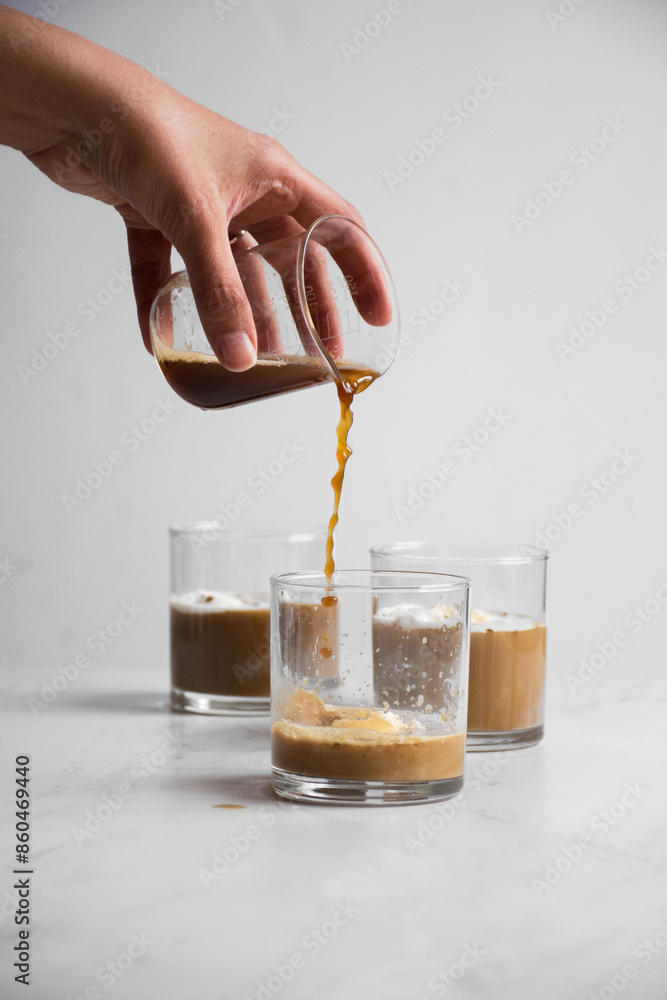 Vertical of a hand pouring coffee into a glass with ice, with additional glasses in the background Vertical of a hand pouring coffee into a glass with ice, with additional glasses in the background