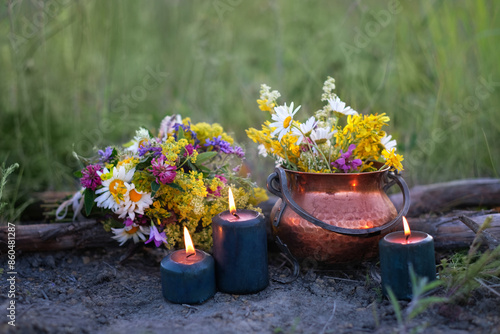 witch copper cauldron with flowers, magic candles on meadow, abstract natural background. herb lore, occult. esoteric ritual, witchcraft, spiritual practice.