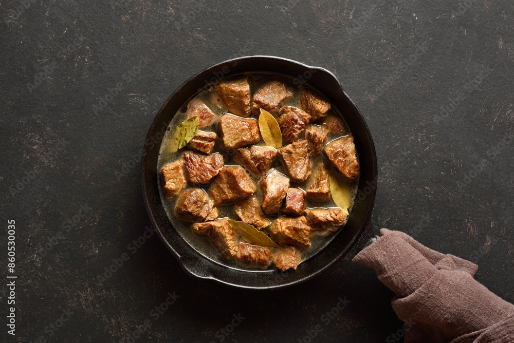 Braised beef in cast iron skillet over dark stone background Braised beef in cast iron skillet over dark stone background