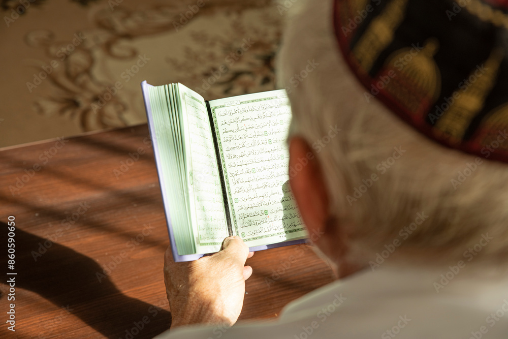 Obraz premium Lifestyle portrait of senior islamic man reading Quran at home. Natural aesthetic light
