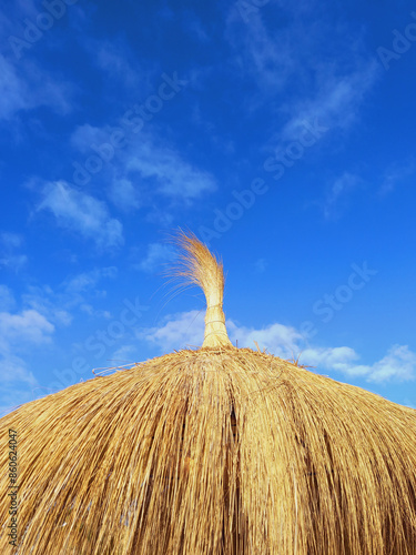 Close up of straw parasol under blue sky. Raffia parasol close up. Heather and wicker texture. Part of the textured hut roof from straw or a reed closeup against an empty and clear sky