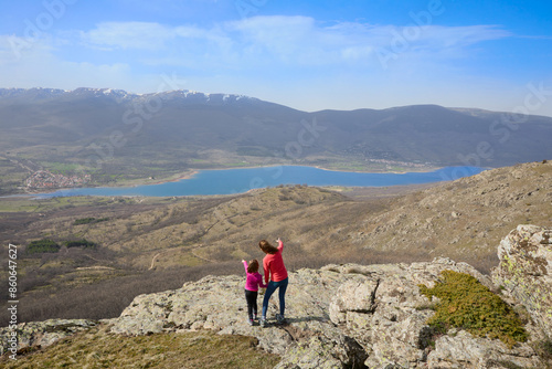 Mother and daughter at the top of the mountain pointing to the Pinilla reservoir, the Lozoya valley and the mountains of the Guadarrama National Park, in Madrid, Spain