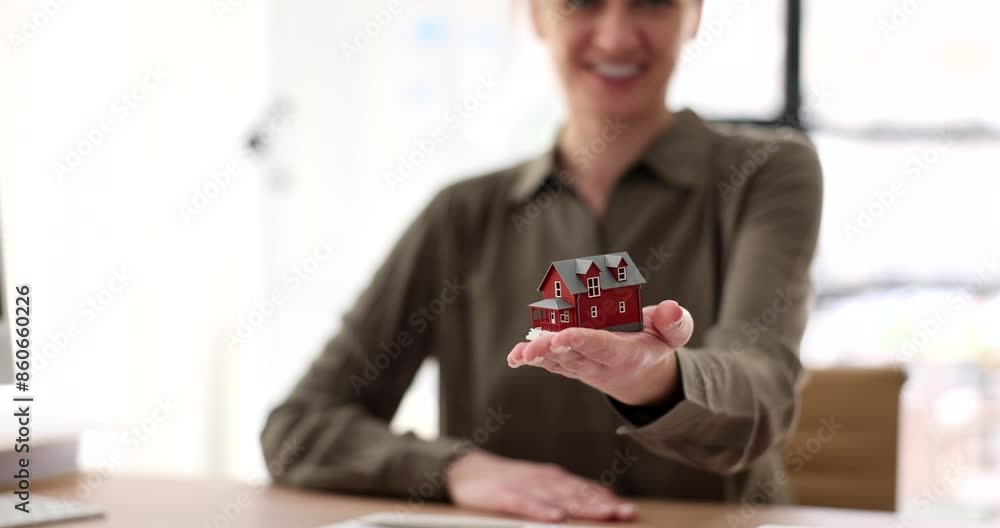Positive female realtor holds house model on palm in agency office slow motion. Real estate agent demonstrates toy apartment to visitors Positive female realtor holds house model on palm in agency office slow motion. Real estate agent demonstrates toy apartment to visitors