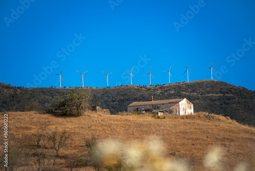 Wind turbines producing electricity in the countryside with ruins in the field. 