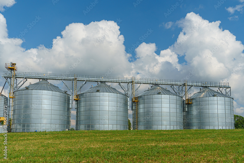 silver silos on agro manufacturing plant for processing drying cleaning and storage of agricultural products, flour, cereals and grain. Large iron barrels of grain. Granary elevator silver silos on agro manufacturing plant for processing drying cleaning and storage of agricultural products, flour, cereals and grain. Large iron barrels of grain. Granary elevator