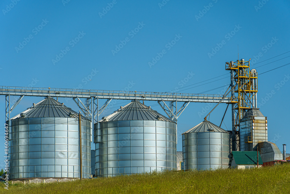 Fototapeta premium silver silos on agro manufacturing plant for processing drying cleaning and storage of agricultural products, flour, cereals and grain. Large iron barrels of grain. Granary elevator