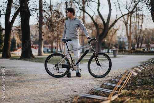 Outdoor portrait of a man standing with a mountain bike in an urban park during the golden hour.