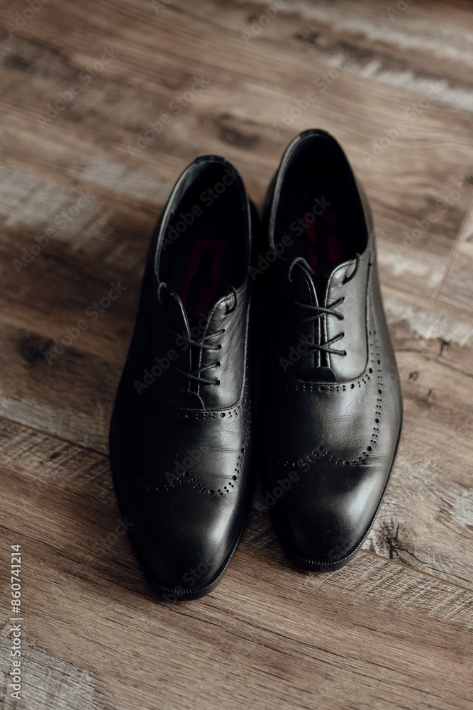 Two black dress shoes with red laces are standing on a wooden floor. The shoes are well-polished and appear to be made of leather. Concept of elegance and sophistication Two black dress shoes with red laces are standing on a wooden floor. The shoes are well-polished and appear to be made of leather. Concept of elegance and sophistication