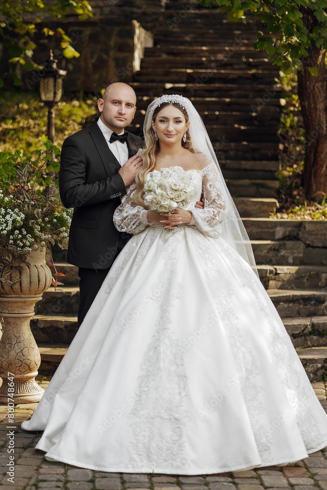 A bride and groom are posing for a picture in front of a staircase. The bride is wearing a white dress and the groom is wearing a suit. The bride is holding a bouquet of flowers A bride and groom are posing for a picture in front of a staircase. The bride is wearing a white dress and the groom is wearing a suit. The bride is holding a bouquet of flowers