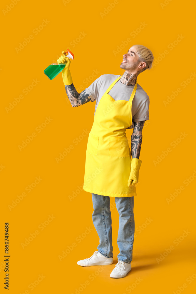 Young tattooed man with bottle of detergent on orange background Young tattooed man with bottle of detergent on orange background
