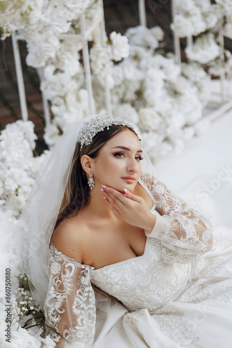 A woman is wearing a wedding dress and a tiara. She is sitting on a bed with a white background