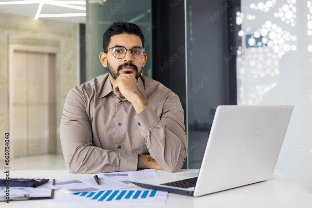 Confident businessman working at desk with laptop and documents in modern office Confident businessman working at desk with laptop and documents in modern office
