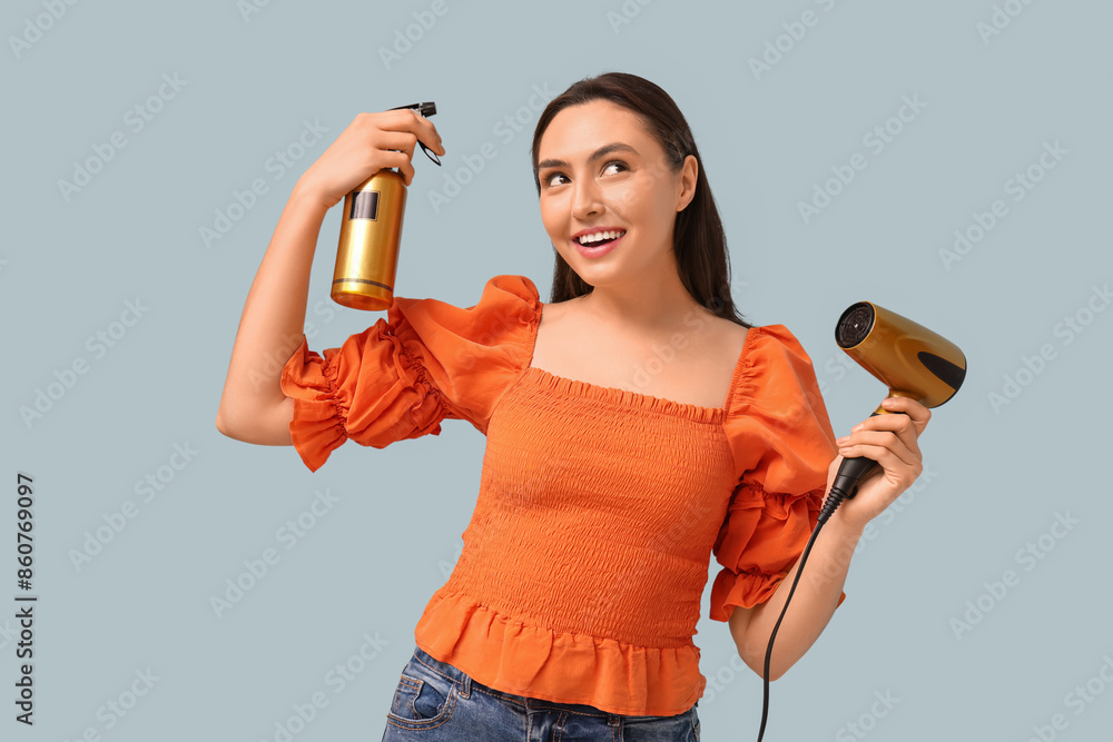 Beautiful young woman with hair dryer and spray on light background Beautiful young woman with hair dryer and spray on light background