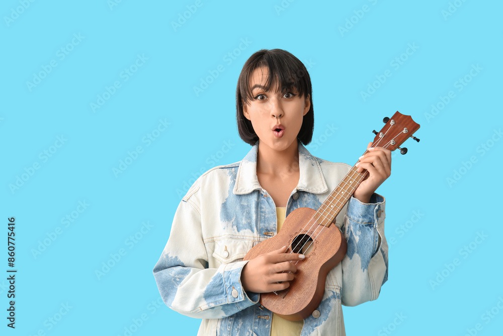 Surprised young woman with ukulele on blue background Surprised young woman with ukulele on blue background