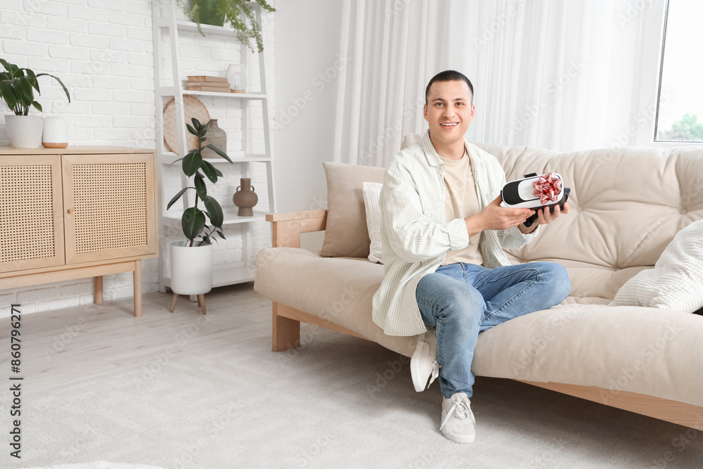 Obraz premium Young man with gift VR glasses sitting on sofa at home
