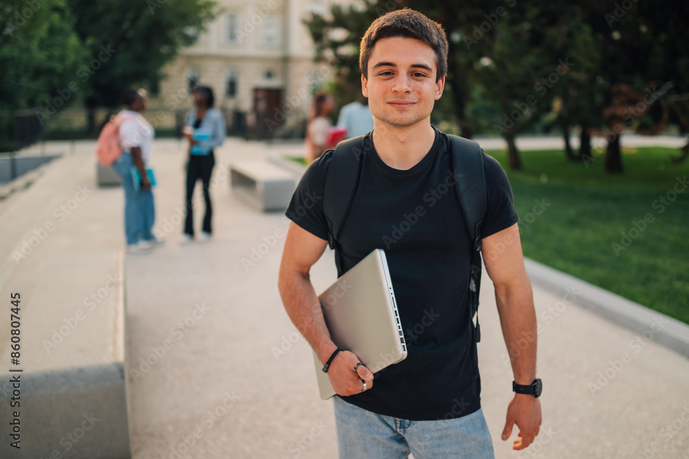 Fototapeta premium Young exchange student boy with laptop at campus looking at camera.