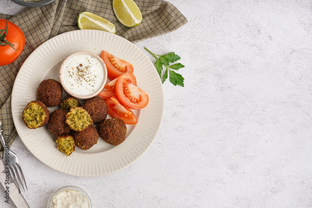 Plate with delicious falafel balls, lime, sauce and tomatoes on light background Plate with delicious falafel balls, lime, sauce and tomatoes on light background