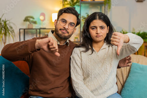 Quadro su tela Portrait of upset young diverse couple showing thumbs down gesture, expressing discontent, disapproval, dissatisfied