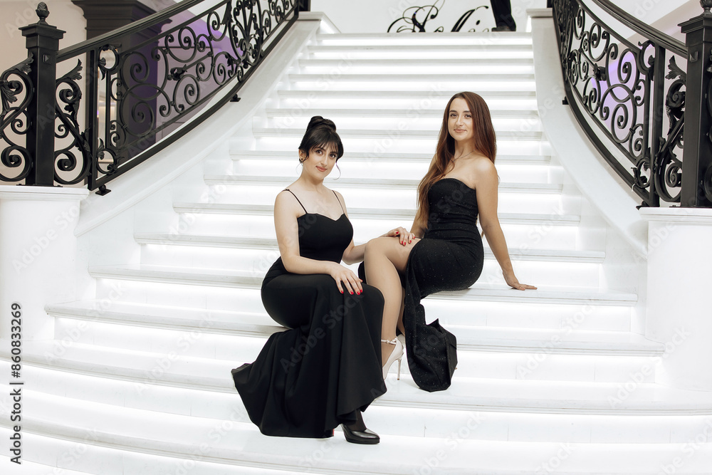 Obraz premium Two women in black dresses are sitting on a white staircase