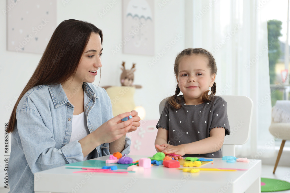 Smiling mother and her daughter sculpting with play dough at table indoors Smiling mother and her daughter sculpting with play dough at table indoors