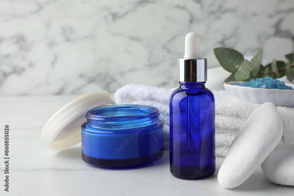 Spa composition. Cosmetic products, sea salt, towel, stones and eucalyptus branch on white marble table Spa composition. Cosmetic products, sea salt, towel, stones and eucalyptus branch on white marble table