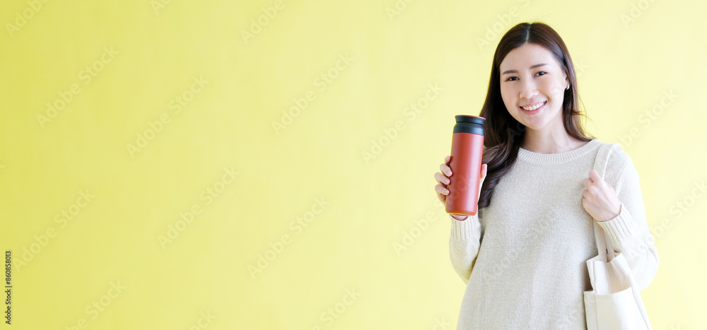 Sustainable and zero waste banner concept, Young asian woman smiling and holding reusable bottle looking at camera while standing on isolated yellow background with copy space Sustainable and zero waste banner concept, Young asian woman smiling and holding reusable bottle looking at camera while standing on isolated yellow background with copy space